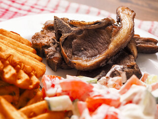 Dinner meal with cooked lamb loin chops, potato lattice and fresh salad with sour cream. Close up....