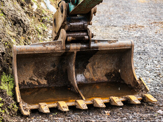 Excavator bucket on the ground. Stone pebble on the ground, soil in the background. Park or house construction work concept. Nobody. Heavy machinery tools and equipment.
