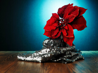 A red flower is wrapped by a silver fabric. The image has a festive and celebratory mood, as it is likely a decoration for a holiday or special occasion. Dark background with blue spot. Still life