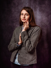 Classic beauty portrait of a young girl in grey business suit on grey painted background. Fashion and beauty. Model has long hair and calm confident face. Feminine soft pose. Relaxed mood