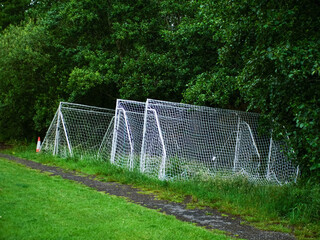 Football or soccer goal posts stacked off training pitch by dark trees. Professional club training field and equipment. World popular sport.