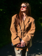 Beautiful young teenager girl in trendy brown jacket, brown background. Model with long hair wearing glasses. Classic beauty. Attractive positive lady enjoy warm sunny day.