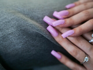 Woman hands with high quality manicure and diamond rings. Pink color nails. Selective focus. Rich and looked after female. Wealthy lady.