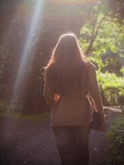 Young and stylish woman walking on a footpath in a park, back to camera. Model enjoys warm sunny day. Fashion and beauty, healthy habit and lifestyle. Selective focus.