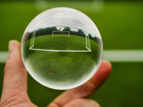 Football or soccer goal posts in glass ball which is hold by a someone hand. Forecasting sport results in popular world sport. Betting on club and national teams concept. Selective focus.