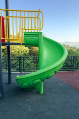 Bright green spiral slide on a playground with mountains and trees in the background, concept of childhood and outdoor fun, vertical