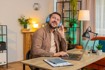 Happy overjoyed businessman sitting at home office desk listening to favorite energetic music...