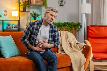 Senior bearded man sitting on couch feeling sudden strong abdominal stomach ache, gastritis...