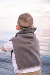 A boy stands quietly, looking out to sea.. Boy looking out to sea. 