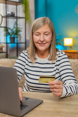 Mature woman shopping online on laptop at home. Caucasian grandmother entering credit card details...