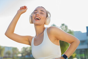 Athletic fitness sport runner girl training exercise listening music on headphones dancing having fun. Workout cardio in park. Young woman jogger enjoying dance. Active sportswoman