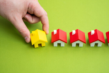 The hand places the yellow house in a row with the others. A unique offer. Milestone achieved through the sale or construction of real estate. Project completion. Importance of choosing the right home