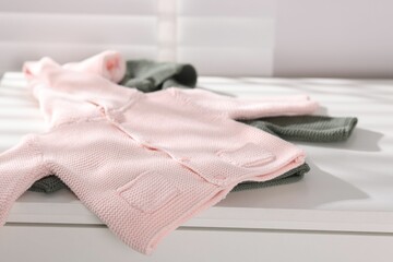 Wool baby sweaters on white nightstand indoors, closeup