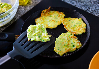 Appetizing zucchini pancakes fried in frying pan in kitchen