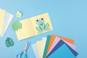 Pop-up paper frog card with scissors on pastel background. Useful for children product brands, arts...
