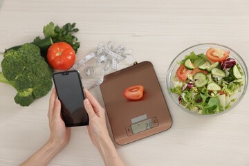 Woman using smartphone at white wooden table with kitchen scale, healthy food and measuring tape,...
