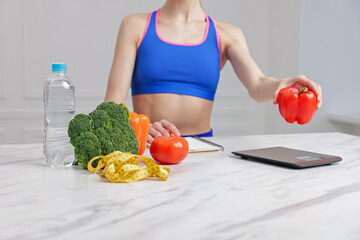 Woman weighting bell pepper on kitchen scale at white marble table indoors, closeup