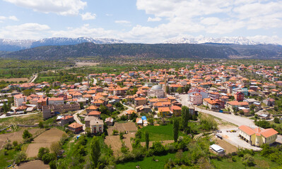 Obraz premium Scenic spring view from drone of Yesildag village with residential houses and mosque in green valley surrounded by mountains with peaks covered with snow, Turkey