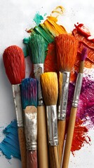 Fototapeta premium A vibrant collection of paintbrushes with colorful bristles resting on a textured canvas, surrounded by various shades of artist's paint.