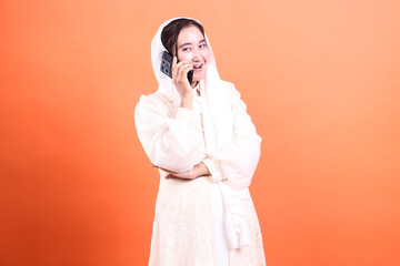 Charming Woman in Hijab Engaging in a Lively Phone Conversation with an Orange Backdrop. isolated on a orange background, creating a vibrant and modern image.