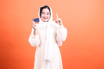 Modern Muslim Woman with Debit Card Smiling, Showing an Idea, isolated on a orange background, perfect for advertisements and promotions.