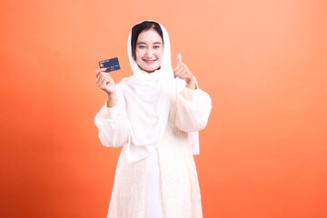 Happy Muslim Woman with Credit Card: A Positive Financial Outlook displayed proudly isolated on a orange background with confidence and cheer.