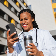 african american woman doctor on break use cellphone in front hospital