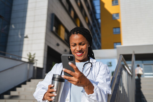 african american woman doctor on break use cellphone in front hospital