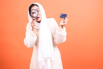 Woman Inspecting Credit Card with Magnifying Glass on Orange Backdrop