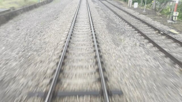 View from the rear window of a moving train looking down at wet railway tracks on a gravel bed. One track splits left, another runs parallel under a cloudy sky after rain