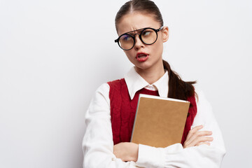 Student girl with glasses looking frustrated, holding a notebook against a plain white background,...
