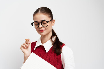 Young woman in oversized glasses holding a document, wearing a red sweater, smiling, on a plain...