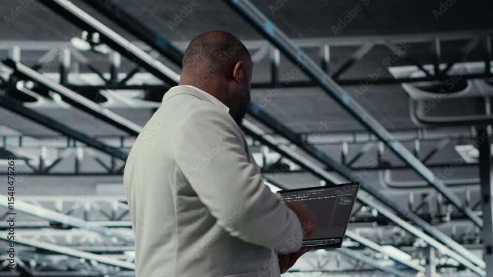 Poster admin walking in data center industrial platform analyzing infrastructure performance outputs on lap