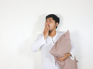 Handsome Asian man yawning while holding a pillow with a sleepy and tired expression
