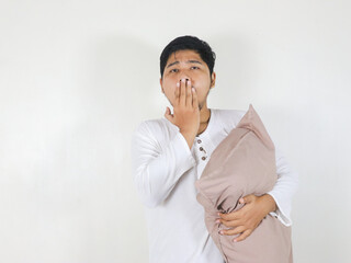Handsome Asian man yawning while holding a pillow with a sleepy and tired expression