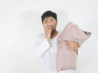 handsome asian man who just woke up holding a pillow and showing a scared face while biting his...
