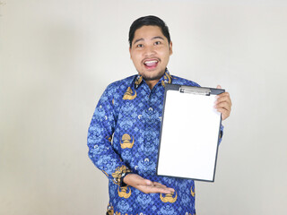 Indonesian civil servant man shows white paper attached to clipboard with excited expression....