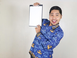Indonesian civil servant man shows white paper attached to clipboard with excited expression....
