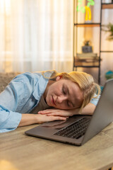 Young woman fights drowsiness at home table desk, lying on laptop computer drifting into tired....