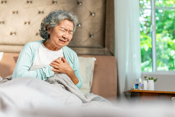 Asian senior woman suffering, feeling pain on chest area and difficulty breathing on the bed....