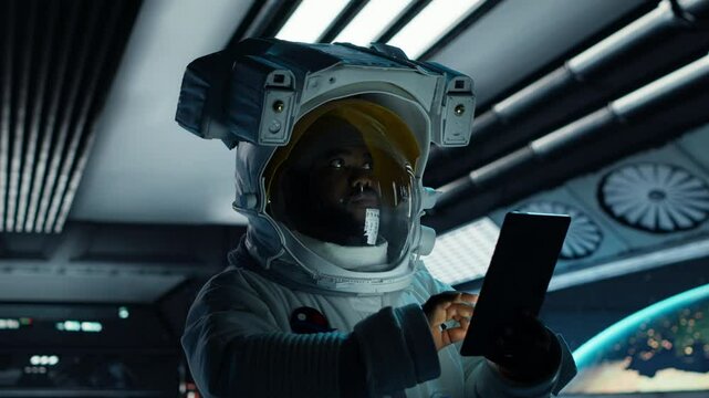 Astronaut wearing spacesuit monitoring mission data on tablet inside futuristic spacecraft. Spacecraft crew member prepares for space travel operations, looking at metrics on device, camera B