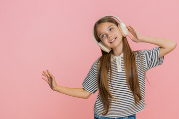 Young child girl joyfully dances while listening to her favorite song in wireless headphones,...