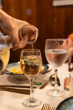 Server pouring white wine into a glass at an upscale dinner with white tablecloths.