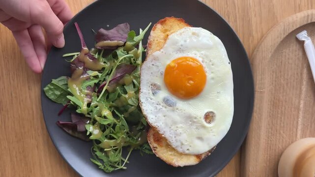 Croque Madame or Grilled cheese with ham and egg on a wooden cutting board. The sandwich is toasted and has a runny yolk and salad in restaurant