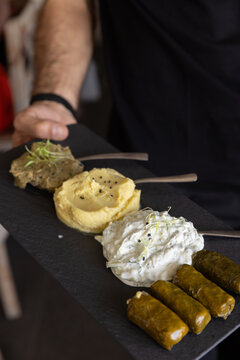 Server in black holding a tray of Greek appetizers including baba ganoush, hummus, dolmas and tzatziki
