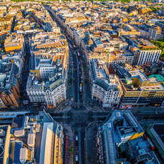 Aerial view of Regent Street in London with its sweeping curve, elegant architecture, red buses, and busy city streets on a clear day.