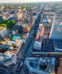 Aerial view of Oxford Street in London with bustling traffic, classic buildings, and red double-decker buses on a sunny, clear day.