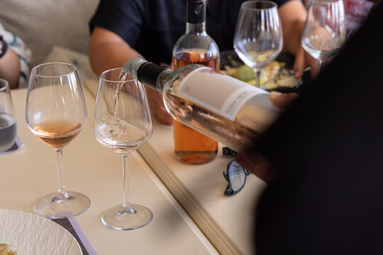 Waiter pouring rose wine for a guest during a group meal at an upscale restaurant or winery. 