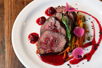 Top view sliced cooked veal served with julienne vegetables and cherry sauce, garnished with...