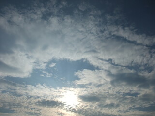 Expansive sky filled with fluffy clouds and soft sunlight peeking through, creating a serene...